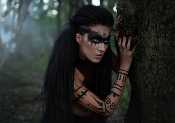 Portret close up of beautiful tribal shaman woman in a foggy forest.Amazon girl near the tree. Soft...