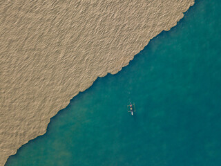 Aerial view of a fisherman fishing in the mouth of the muddy Comoro river with the green coral reef ocean in Dili, Timor-Leste