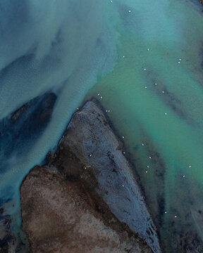 Aerial view of beautiful blue and green patterns, and swans swimming in the water of glacial river H&radic;&copy;raosvotn in North Iceland.