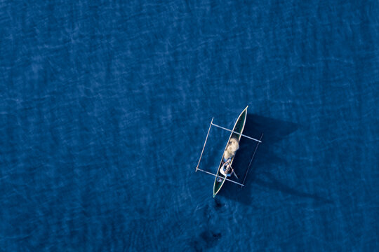 Aerial view of a fisherman and his mirror shadow fishing using a pirogue boat on deep blue ocean waters during sunrise in Dili, Timor-Leste