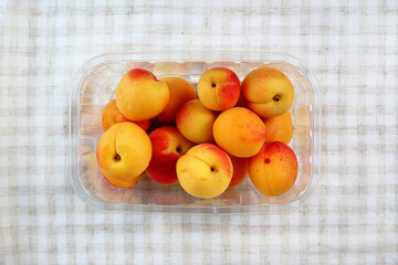 Apricots in a bowl against a background of checkered pastel fabric.