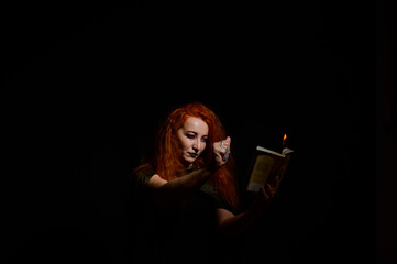 An ominous witch sets her spell book on fire with the power of thought. Red-haired woman conjures...