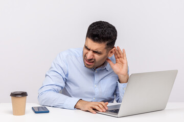 Confused businessman sitting office workplace, leaning towards laptop and holding hand near ear trying to hear better, listening for quiet noise. indoor studio shot isolated on white background