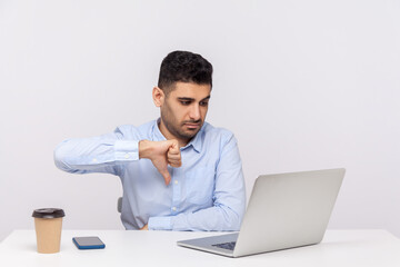 Dislike! Businessman sitting office workplace showing thumbs down gesture to laptop screen,...