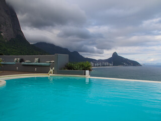 Rio de Janeiro view from the pool: green mountains, ocean, clouds and sun.