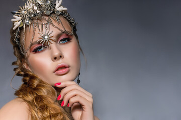 Close up portrait of a young beautiful blonde woman wearing a crown and costume jewelry on a gray background