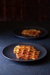 toasted Viennese zucchini waffles on two black plates on a dark concrete background, minimalism.