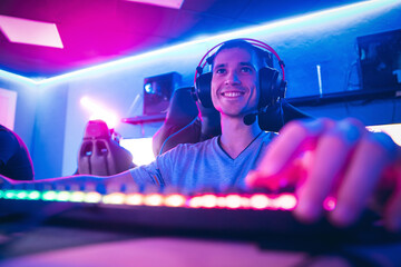 Happy professional cyber sport gamer playing online computer game with headphones, Blurred Red and Blue background