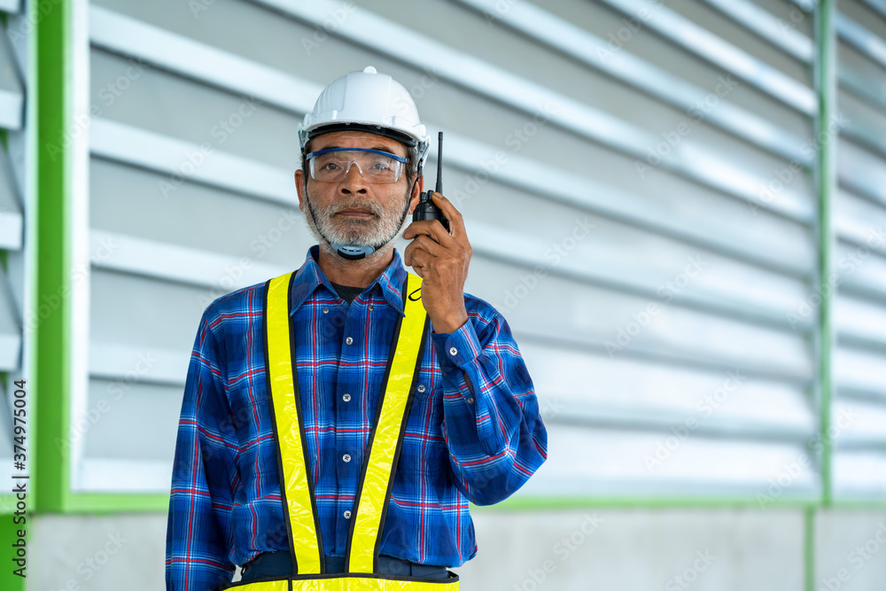 Poster engineer using walkie-talkie while colleagues discussing in warehouse.