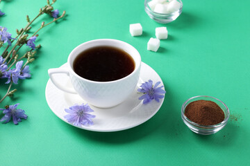 Chicory beverage in white cup, with concentrate and flowers on green background. Healthy herbal beverage, coffee substitute, Closeup