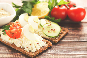 Crispbread with cream cheese, eggs and vegetables on brown wooden table