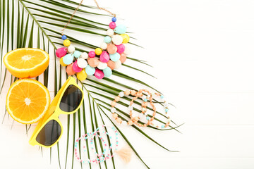 Beautiful bracelets, necklace with sunglasses, orange, fruit and palm leaf on white wooden background