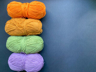 Colored yarn for knitting on a black background. Balls of yarn in purple, green and orange colors. Photo from above. Crocheting and knitting, needlework. The concept of creating products.