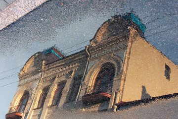 An inverted reflection of the top of an old building on the wet asphalt after rain.