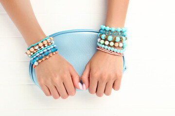 Female hands with bracelets holding handbag on white wooden background