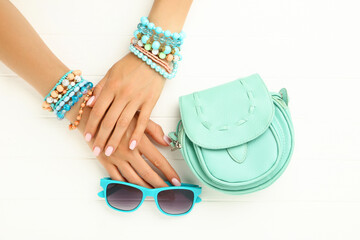 Female hands with bracelets, sunglasses and handbag on white wooden background