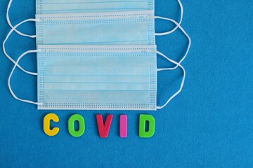 Blue medical surgical mask on blue background, medical protective mask and inscription COVID
