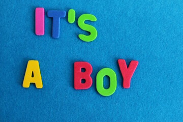 It Is A Boy, Top view of textured letters with it's a boy lettering on blue 
