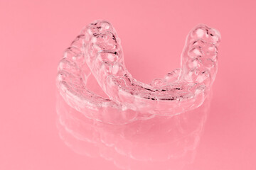 Two Invisible dental teeth aligners on the pink background. Orthodontic temporary removable braces...