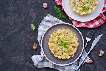 Portion mini tart with chicken, zucchini and fried onions on shortcrust pastry with sour cream and eggs filling on a clay plate on a dark concrete background. Savory pastry recipes.