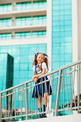 A schoolgirl in a blue school uniform, standing in the background of the school, with glass walls.
