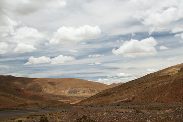 Desert landscape. Asphalt highway along the arid valley and brown mountains under a beautiful cloudy sky. 