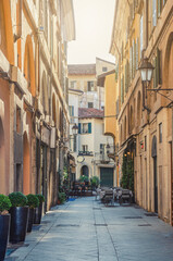 Typical italian street with old colorful buildings with shutter windows, street lights at wall, restaurant tables, Brescia city historical centre, vertical view, Lombardy, Northern Italy