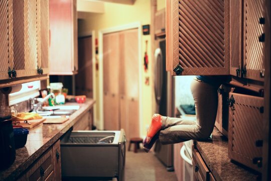 Girl on the counter with her face in the cabinet, looking for something to eat.