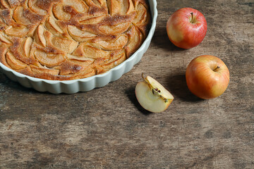 Traditional french homemade apple pie in a white ceramic baking form and autumn apples on old dark...