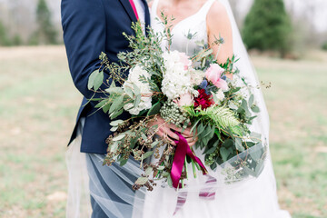 Beautiful Wildflower Wedding Bouquet with Bride and Groom in the Background in a Green Field