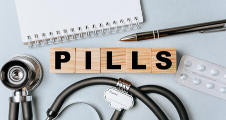 Wooden block form the word PILLS with stethoscope, pills, notepad, pen on the doctor's desktop....