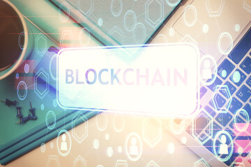 Blockchain theme hologram drawings over computer on the desktop background. Top view. Multi...