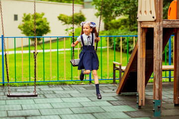 schoolgirl in school uniform, swinging on a swing in a children's Park