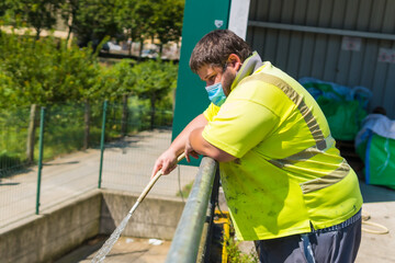 Fototapeta premium Worker in a recycling factory or clean point and garbage with a face mask and with security protections, new normal, coronavirus pandemic, covid-19. Portrait of worker cleaning with hose
