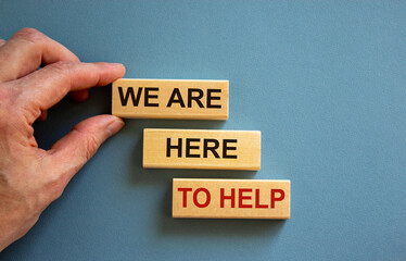 Wooden blocks with text 'we are here to help'. Male hand. Beautiful blue background, copy space. Business concept.