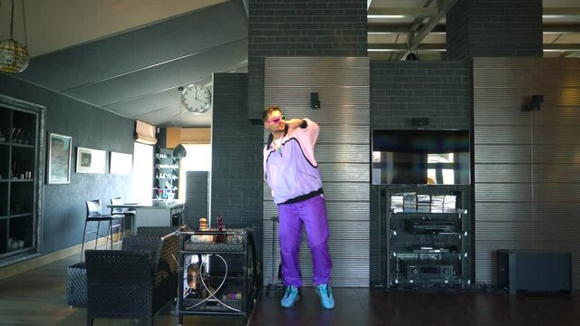 A freak guy in a fashionable suit from the 80s and 90s is dancing at home and grimacing at the camera, a funny cheerful young man, he is filming for social networks, handsome gay, colored clothes.