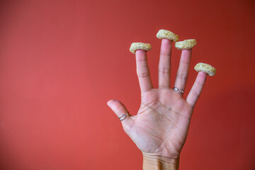 Arm with fingers wore cereal rings on red background