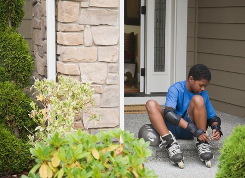 Boy (10-11) fastening inline skates in front of house