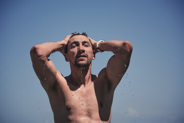 Portrait of a tanned man coming out of a swimming pool with water dripping from his body. In the background in blue sky.