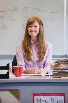 Portrait of smiling teacher sitting at desk in classroom