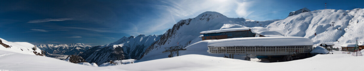 Mountain panoramic view with snow picks, bright blue sky and ski lift station
