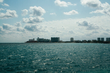 Obraz premium Tourism. Seascape. View from a boat sailing the turquoise color water ocean. The blue sea, coastline and Cancun city buildings in the horizon, in a sunny summer day.