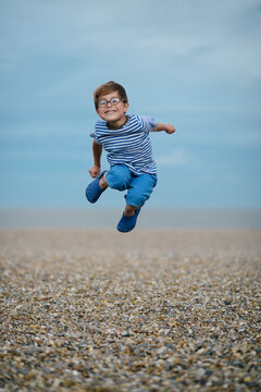 A caucasian boy jumps for joy on a stony beach