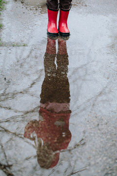 girl in red boots reflected in rain puddle
