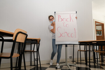 Girl wearing a medical mask in an empty classroom with back to school on whiteboard, new normal back to school