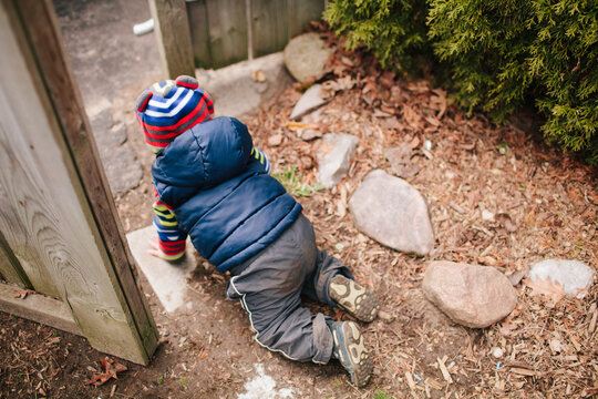 Little boy crawling out of a gate escaping with a vest and hat on.