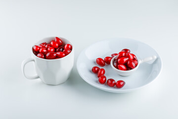 Cornel berries in scoop, plate and cup high angle view on a white background