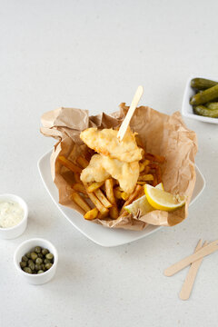 Fish and chips on brown paper with lemon wedges
