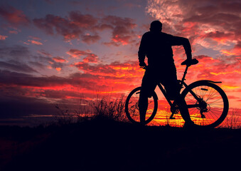Obraz premium cyclist with a bicycle, in the background fiery sunset.