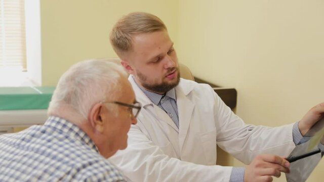 Male neurologist looking at an x-ray picture with an elderly patient.